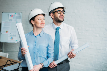 happy architects standing at modern office with building plans and looking away