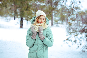 Obraz premium Young beautiful blond girl outdoors in winter hands raised to head looking at camera. Winter. A girl is walking in a winter fir forest. Portrait. Space for text close-up.