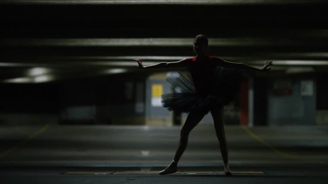 Young ballet dancer balances on pointe in a car park, in slow motion