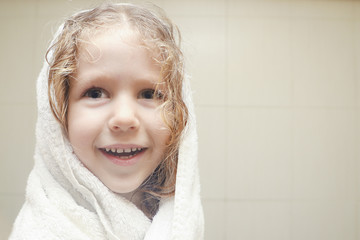 Little curly girl in towel in bathroom after shower.