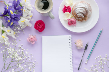 Coffee, clean notebook, eyeglasses and flower on purple table from above. Female working desk. Cozy breakfast. Flat lay style. top view. Delicious breakfast, sweet rolls