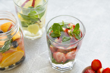 Detox infused water with sliced strawberry, oranges, lemons and mint on light concrete background, close up