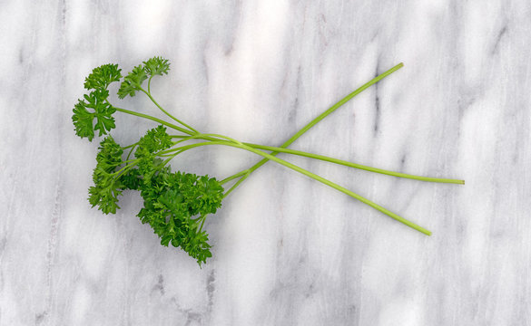 Top view of several curly parsley sprigs on a gray marble cutting board.