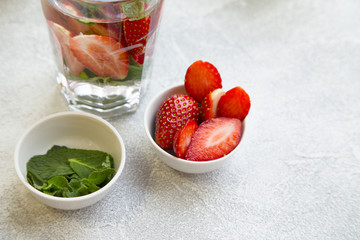 Ingredients for making detox water: bowls with strawberry and mint, light concrete background
