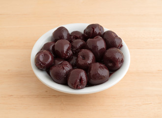 A small white bowl of sweet pitted cherries on a wood table.