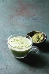 Cup of matcha latte with bowl of matcha tea over grey green texture background. Copy space.