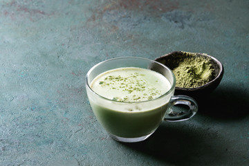 Cup of matcha latte with bowl of matcha tea over grey green texture background. Copy space.