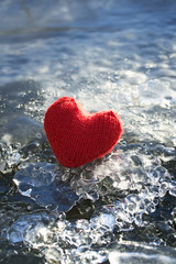Fototapeta premium a symbol of love and warm holiday red knit heart on a sparkling cold ice