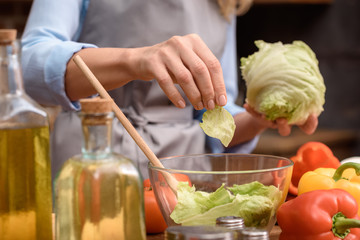 cropped image of woman adding salad leaves to salad