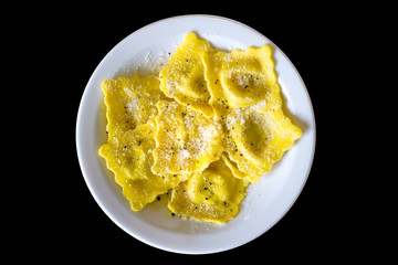 Seasoned dish of italian ravioli (dumplings) with parmesan and black pepper on black background