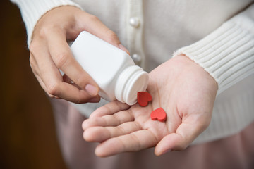Female holding a white pill bottle and red pills in heart shape.