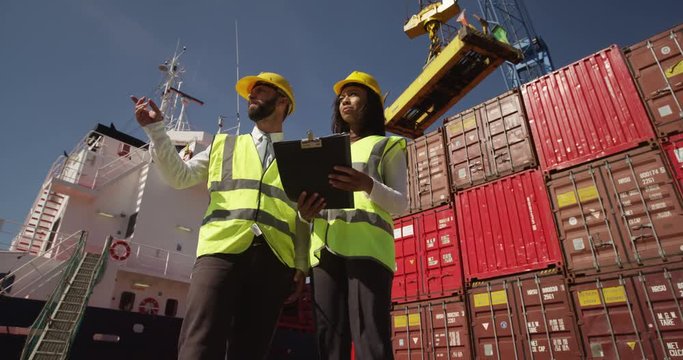 Businesswoman and dock worker shake hands at a busy shipyard. Shot on RED Epic.