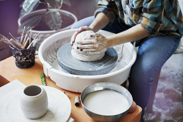 Fototapeta na wymiar Ceramic studio, craft working process with clay potter's wheel, close-up of hands doing a pot or a vase, object