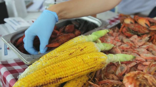 Seller puts boiled crayfish and mussels in disposable dish in the street cafe