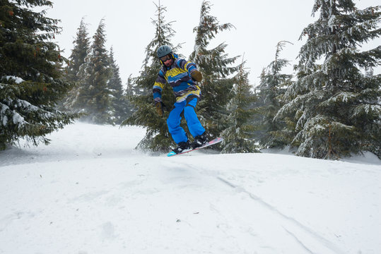 Snowboarder jumps amidst huge snow-covered fir trees
