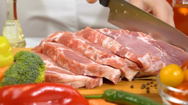 Woman hands slicing fresh raw meat for cooking with vegetables in kitchen. Slow motion shot.