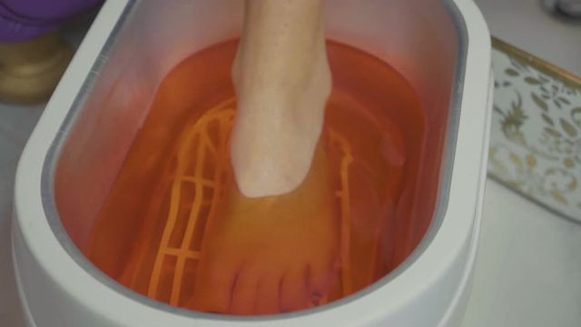 Wax bath for feet at beauty spa salon. Close-up in slow motion.