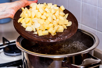 Hand adds raw potato pieces in boiling water