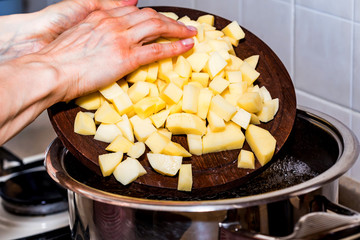 Hand adds raw potato pieces in boiling water