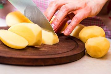 Female hands cut potatoes on wooden board