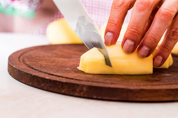 Female hands cut potatoes on wooden board