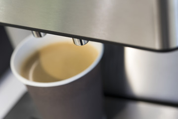 Cardboard cup with coffee on coffee machine close up