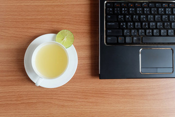 Top view, freshly Lime juice in a white cup, and laptop on wooden floor