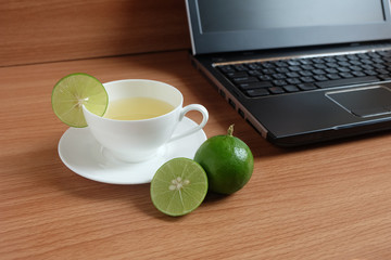 freshly Lime juice in a white cup, and laptop on wooden floor
