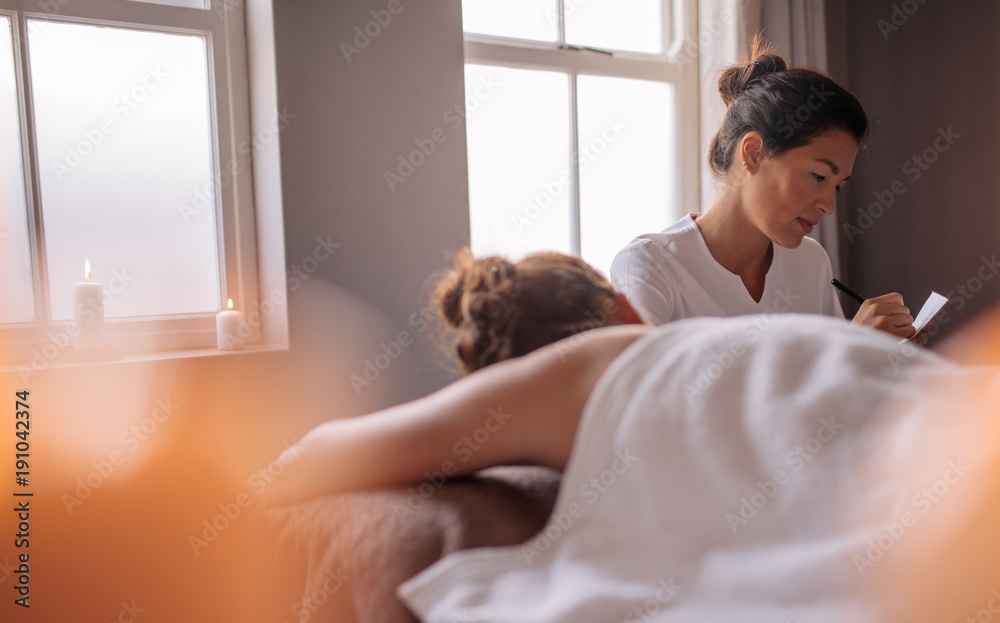 Wall mural Masseuse writing the requirements of female client at beauty spa