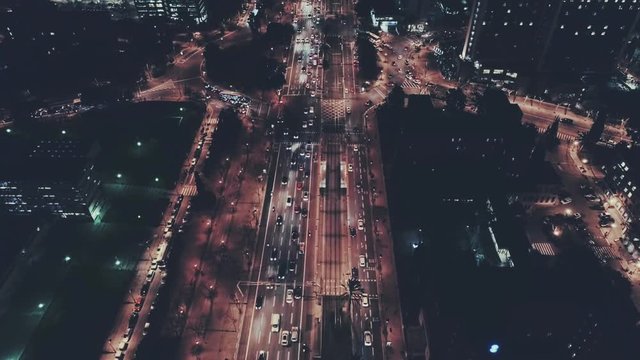 Night time commuter traffic with cars and business offices, aerial drone footage flyover of impressive big city life with lights and road junctions on highway urban city planning