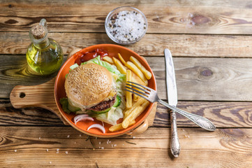 Home-made hamburger with beef, tomato and salad on a plate with fried potatoes. Wooden background