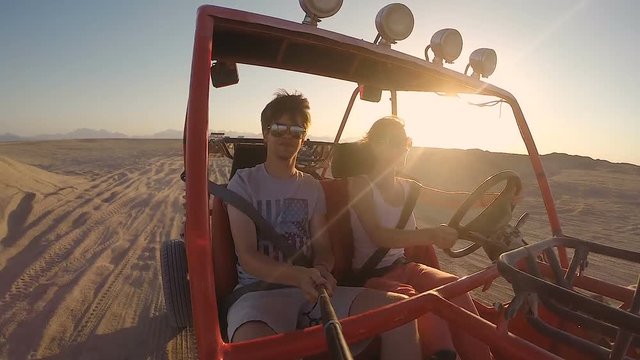 Young traveling couple driving through the desert in a dune buggy at sunset