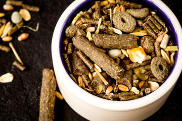 dry food for rodents in bowl dark background top view
