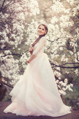 Fototapeta premium Beautiful young woman with crown in blossom magnolia garden. Spring.