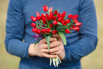 Flowers lazoriki. Bouquet of Red tulips in the hands of the men in blue clothing.
