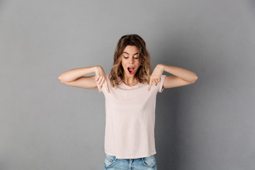 Shocked happy woman in t-shirt pointing and looking down