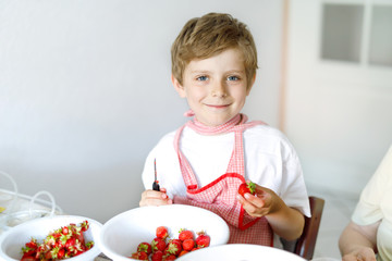 Little blond kid boy helping and making strawberry jam in summer