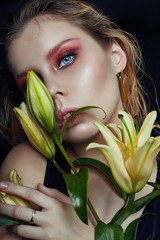 Closeup portrait of woman with flowers lilies in his hands, bright contrasting makeup on the girl's face. Wet hair and clean natural leather