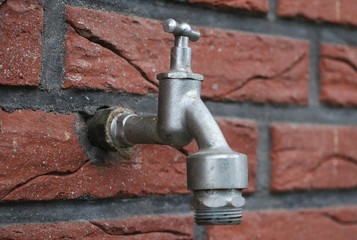 Wasserhahn an der Hauswand im Garten