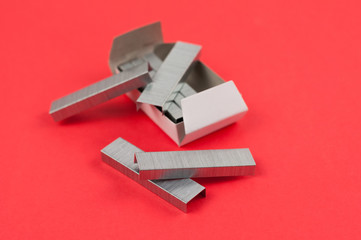 Stationery new metal clips for stapler poured out of cardboard box on red background