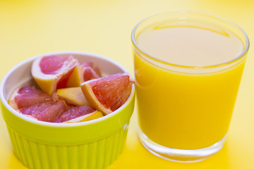 Delicious breakfast: a bowl of sliced grapefruit and a glass of orange juice on a yellow background with copy space, top view