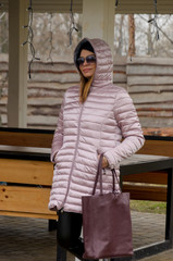 attractive woman is standing in a quilted winter pink jacket near a bessie in a country complex. Rest of the day off