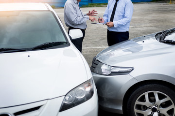Insurance agent writing on clipboard while examining car after accident claim being assessed and processed.