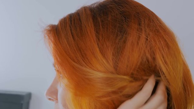 Close up shot of woman fixing orange hair at hairdressing salon. Beauty and fashion concept