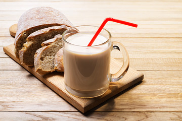 Glass mug with drinking yoghurt and sliced rye bread with a cutting wooden board on a wooden surface