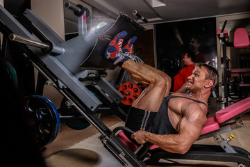 Fototapeta na wymiar Athletic bodybuilding man in gym leg lifting weight.