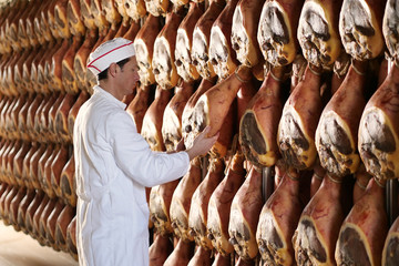 In a ham factory, a man in charge of quality control walks between the hams and controls, the...