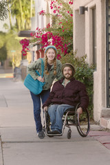 Fototapeta na wymiar Young Woman and Man in Wheelchair on Sidewalk