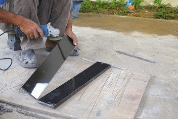 Worker cutting floor tiles with angle grinder at construction site