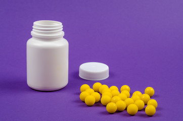 Plastic bottle with medicines without a lid and yellow pills next to her on a purple background.